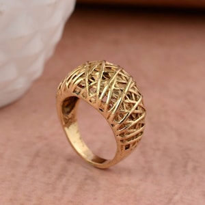 May include: A gold-toned ring with a geometric, woven design. The ring is wide and has a rounded top.