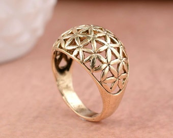 Puede incluir: Anillo de color dorado con un diseño de flor geométrico. El anillo está hecho de metal y tiene una banda ancha.