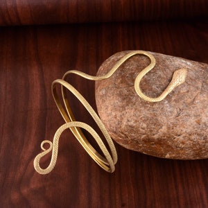Peut inclure: Bracelet en forme de serpent doré avec un design enroulé. Le bracelet est en métal et a une finition texturée.