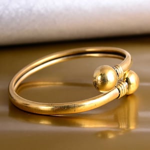 May include: A gold bangle bracelet with two round decorative accents. The bracelet is made of a smooth, shiny metal.