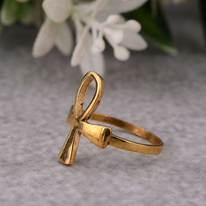 May include: A gold-toned ring featuring an Ankh symbol design. The ring is made of metal and has a plain band.