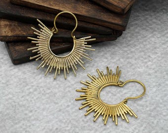 Peut inclure: Une paire de boucles d'oreilles créoles dorées avec un motif soleil. Les boucles d'oreilles sont en métal et ont une forme circulaire avec une série de pointes rayonnant vers l'extérieur.