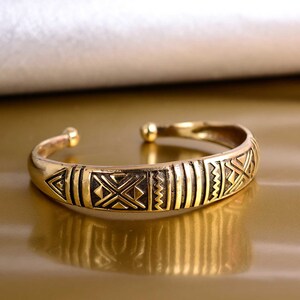 May include: A gold-toned bangle bracelet with a geometric pattern. The bracelet is made of metal and has a simple, elegant design.