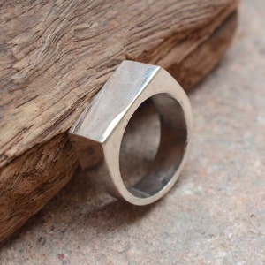 May include: A silver ring with a geometric, octagonal shape. The ring is made of a smooth, polished metal and has a simple, modern design.