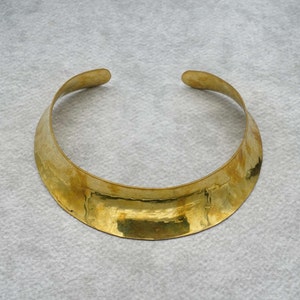 Könnte beinhalten: Eine goldfarbene Metallkette mit einem breiten, flachen Band. Das Band ist leicht gebogen und hat eine gehämmerte Textur.