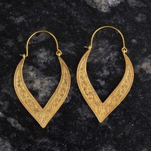 May include: A pair of gold-tone earrings with a delicate, intricate design. The earrings are shaped like a teardrop and have a v-shaped opening at the top.