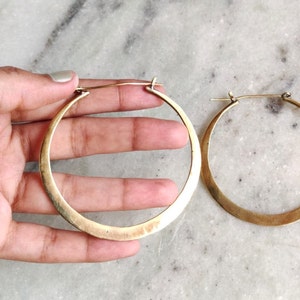 Könnte beinhalten: Ein Paar große, goldfarbene Creolen. Die Ohrringe sind aus dickem, flachem Metall gefertigt und haben ein schlichtes, minimalistisches Design.