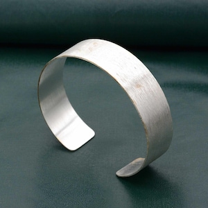 May include: A silver metal cuff bracelet with a brushed finish. The bracelet is open and has a slightly curved shape.