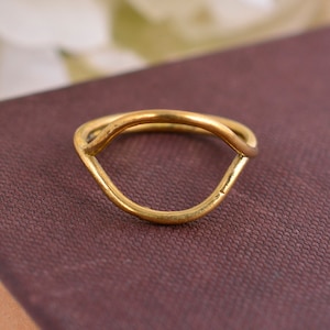 Puede incluir: Un anillo de oro simple con un diseño abierto y curvado. El anillo está hecho de una sola pieza de metal y tiene un acabado liso y pulido.