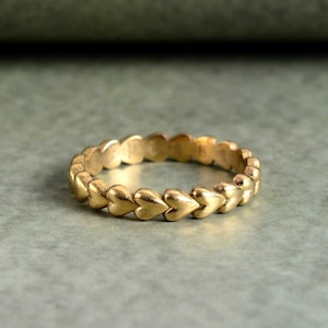 May include: A gold ring with a band of small, connected heart shapes.