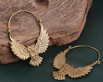 May include: A pair of gold-toned hoop earrings with an owl design. The owls have detailed wings and are facing forward.
