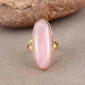 May include: A gold ring with a large oval-shaped pink gemstone. The ring is set in a simple, elegant design.