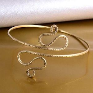 May include: A gold-toned metal bracelet with a hammered finish and a unique, abstract design. The bracelet is open and adjustable.