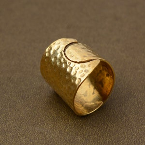 May include: A gold-toned ring with a hammered texture and a unique open design. The ring is made of metal and has a smooth, polished finish.