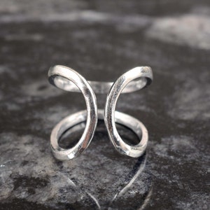 May include: A silver ring with a unique, open design featuring two intersecting circles.