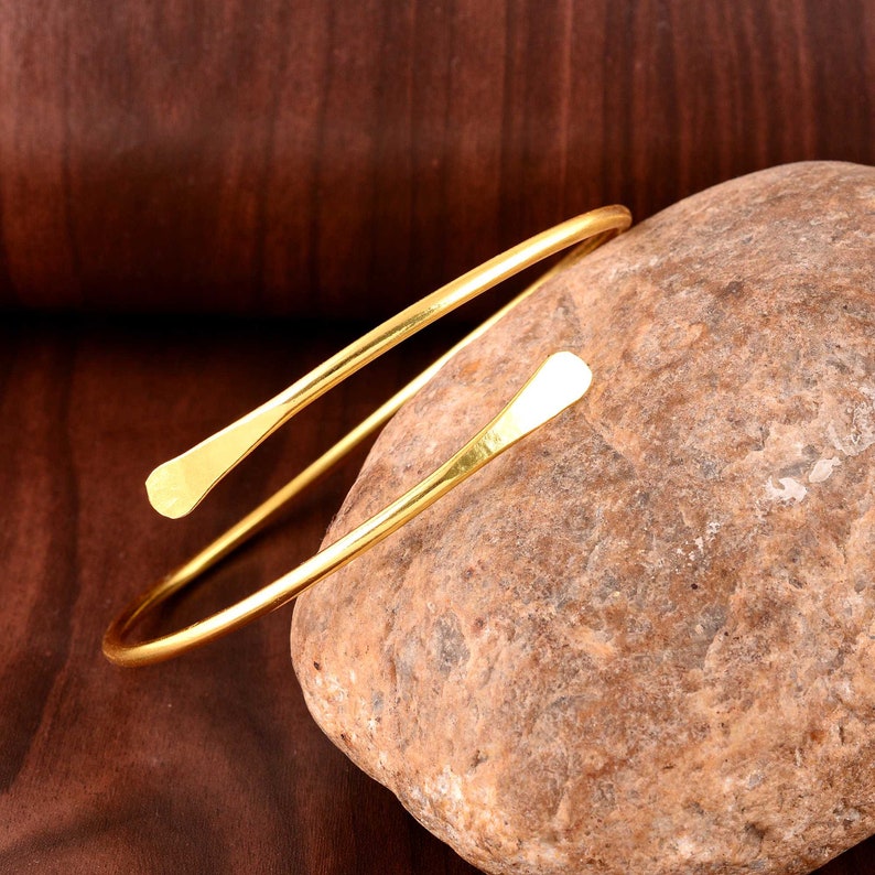 Peut inclure: Un bracelet jonc simple en or avec des extr&eacute;mit&eacute;s arrondies. Le bracelet est fait d'une seule pi&egrave;ce de m&eacute;tal et est ouvert d'un c&ocirc;t&eacute;.