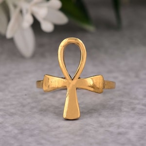 May include: A gold-coloured ring featuring an Ankh symbol, a traditional Egyptian hieroglyph.