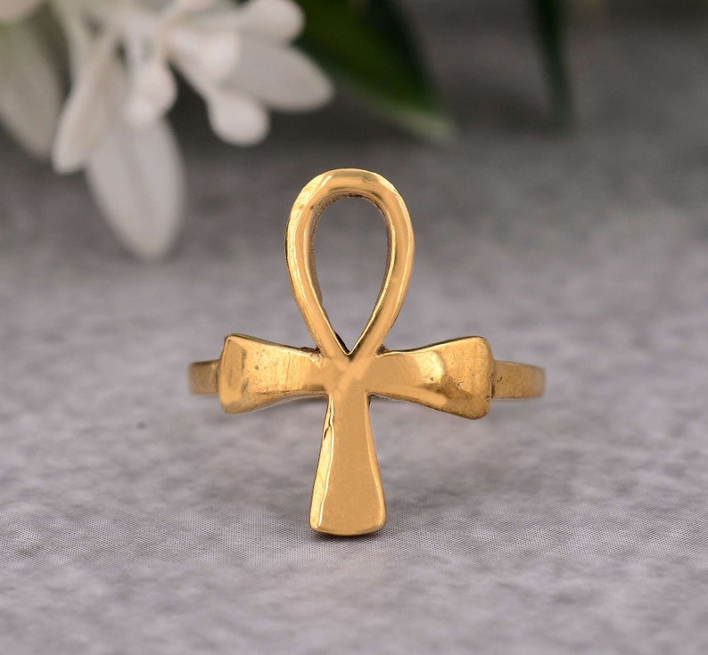 May include: A gold-coloured ring featuring an Ankh symbol, a traditional Egyptian hieroglyph.