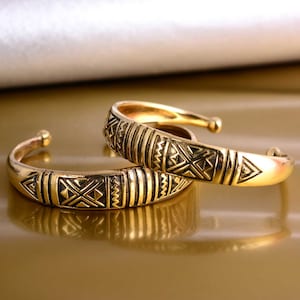 May include: Two gold-toned metal bangles with a geometric pattern. The bangles are stacked on top of each other.