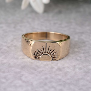 Può includere: Un anello a sigillo in oro con un design a sole in rilievo. L'anello è in stile semplice e moderno.