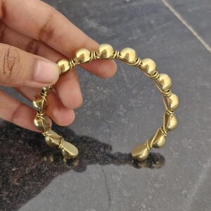 May include: A gold-toned bangle bracelet with a series of round beads connected by wire.