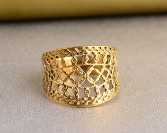 Puede incluir: Un anillo de color dorado con un diseño delicado, intrincado y calado. El anillo es ancho y tiene una forma redondeada.