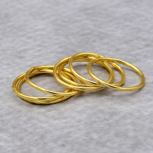 May include: A set of five gold-colored metal bangles stacked together. The bangles are smooth and shiny.