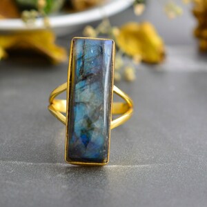 May include: A gold ring with a large, rectangular, iridescent blue labradorite gemstone.