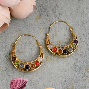 Peut inclure: Une paire de boucles d'oreilles créoles en or avec un motif de croissant de lune. Chaque boucle d'oreille présente une rangée de pierres précieuses colorées.