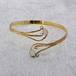 May include: A gold-toned bangle bracelet with a delicate, swirling design. The bracelet features two clear, teardrop-shaped stones.