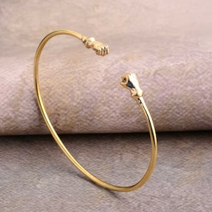 May include: A gold-toned bracelet with two hands clasped together at the ends.
