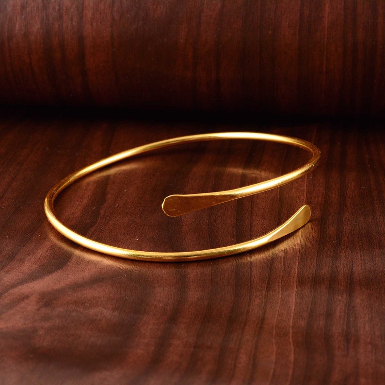 Peut inclure: Un bracelet jonc en m&eacute;tal dor&eacute; avec un design simple et ouvert. Le bracelet est fait d'une seule pi&egrave;ce de m&eacute;tal continue qui est pli&eacute;e en cercle puis tordue &agrave; une extr&eacute;mit&eacute; pour cr&eacute;er une forme asym&eacute;trique unique.