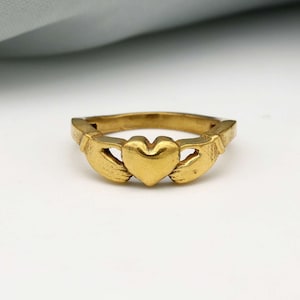 May include: A gold-coloured Claddagh ring with two hands clasped around a heart.