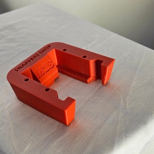 Op de afbeelding: Een rode 3D-geprinte batterijhouder met de tekst "Snappers Shop" en "MLB" aan de zijkant.