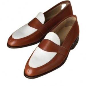 May include: A pair of brown leather loafers with white leather accents. The loafers have a rounded toe and a slip-on design.