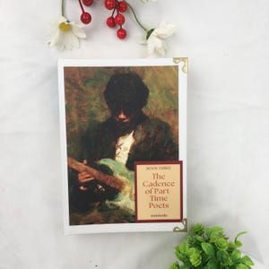 May include: A hardback book titled "The Cadence of Part-Time Poets" featuring a painting of a person playing a guitar. The book has a white cover with gold corner protectors. The book is Book Three in a series.