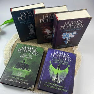 May include: A collection of hardcover books titled "James Potter" with various sub-titles, including "Hall of El Crossing", "Crimson", "The Morrigan Web", "The Vault of Destinies", and "Curse of the Gatekeeper". The books have decorative gold corners.