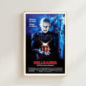 May include: A vintage movie poster for the horror film Hellraiser. The poster features a dark blue background with a menacing figure in the centre. The figure is wearing a black leather outfit with a metal headpiece and holding a small, glowing box. The text on the poster reads "Demon to some. Angel to others. Hellraiser. He'll tear your soul apart."