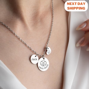 May include: A silver necklace with three round charms. The charms are engraved with the words "Jack", "Hello World", and a cartoon face with glasses.