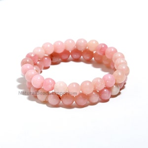 Puede incluir: Un brazalete de doble cadena hecho con cuentas de ópalo rosa. El brazalete está hecho con cuentas redondas y tiene una longitud aproximada de 18 cm.