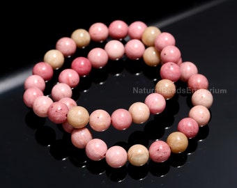 May include: Two bracelets of pink and cream-colored gemstone beads. The beads are round and have a polished finish. The bracelets are displayed on a black surface. The text "NaturalBeadsEmporium" is visible in the image.