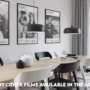 May include: A dining room with a wooden table and six chairs. The table is set with a black vase, a white vase, and a stack of books. There are three black pendant lights hanging above the table. The walls are decorated with three movie posters: "Death Proof", "Rocky", and "Scarface".