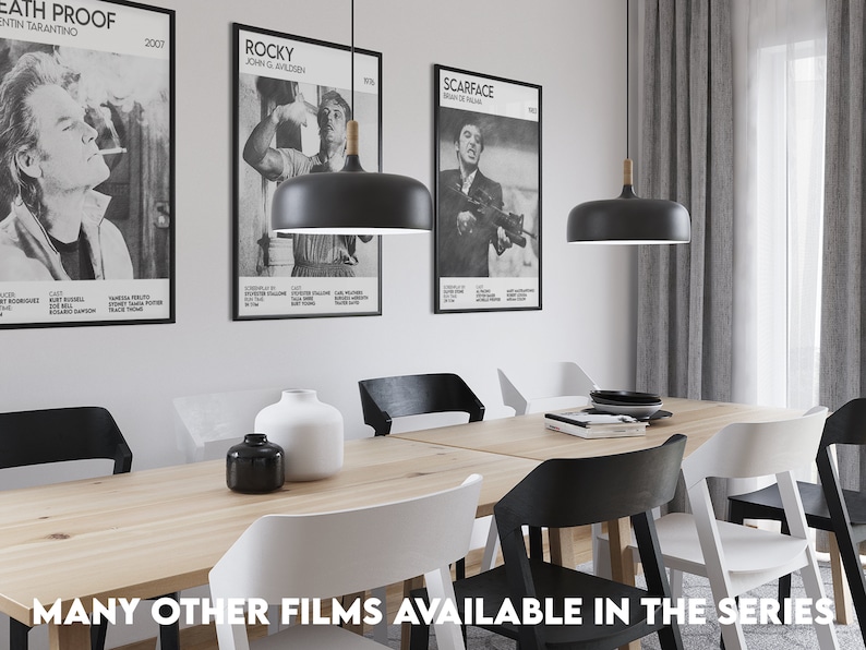 May include: A dining room with a wooden table and six chairs. The table is set with a black vase, a white vase, and a stack of books. There are three black pendant lights hanging above the table. The walls are decorated with three movie posters: "Death Proof", "Rocky", and "Scarface".