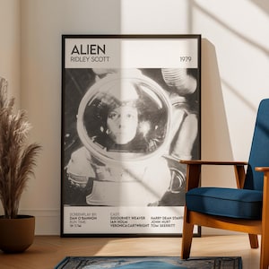 May include: A framed black and white poster for the film "Alien" by Ridley Scott, released in 1979. The poster features a portrait of Sigourney Weaver in a spacesuit helmet. The poster also includes the film's cast and crew.