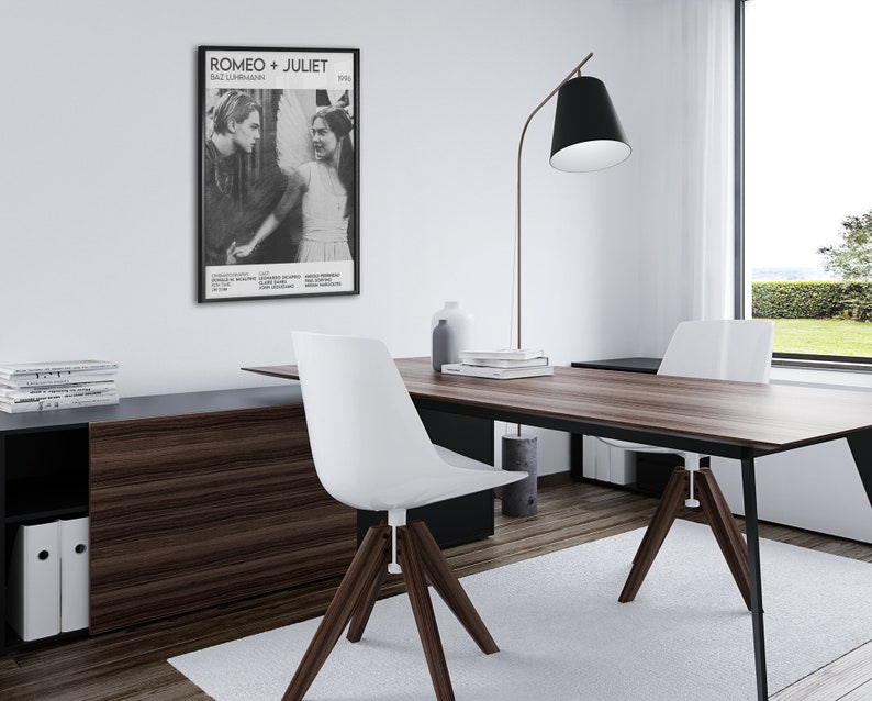 May include: A black and white movie poster for the film "Romeo + Juliet" featuring Leonardo DiCaprio and Claire Danes. The poster is framed and hanging on a white wall in a home office.