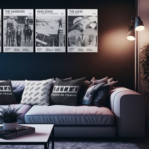May include: A living room with a white couch and black throw pillows. The pillows have a film reel design and the text "Flicks in Frame". There are four black and white movie posters on the wall behind the couch. The posters are for the movies "Jaws", "The Warriors", "King Kong", and "The Mask".