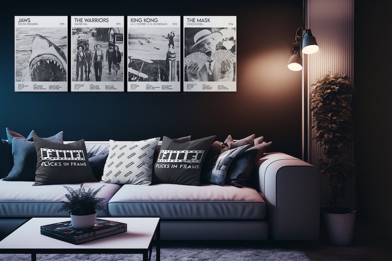 May include: A living room with a white couch and black throw pillows. The pillows have a film reel design and the text "Flicks in Frame". There are four black and white movie posters on the wall behind the couch. The posters are for the movies "Jaws", "The Warriors", "King Kong", and "The Mask".