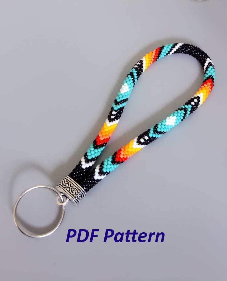 May include: A beaded key chain with a turquoise, orange, yellow, white, and black geometric pattern. The key chain has a silver ring and a silver clasp. The text "PDF Pattern" is printed below the key chain.