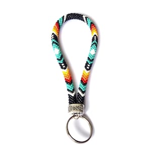 May include: A beaded key chain with a black, white, turquoise, orange, and red geometric pattern. The key chain has a silver key ring attached.