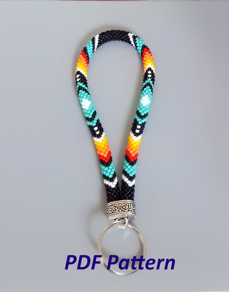 May include: A beaded key chain with a black, white, turquoise, orange, and red geometric pattern. The key chain has a silver ring and a silver clasp.
